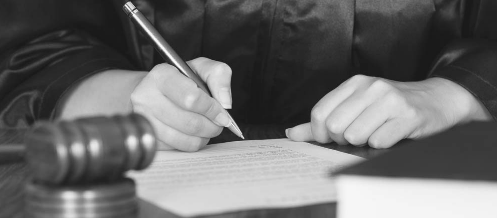 A person signing a document with a gavel in the foreground